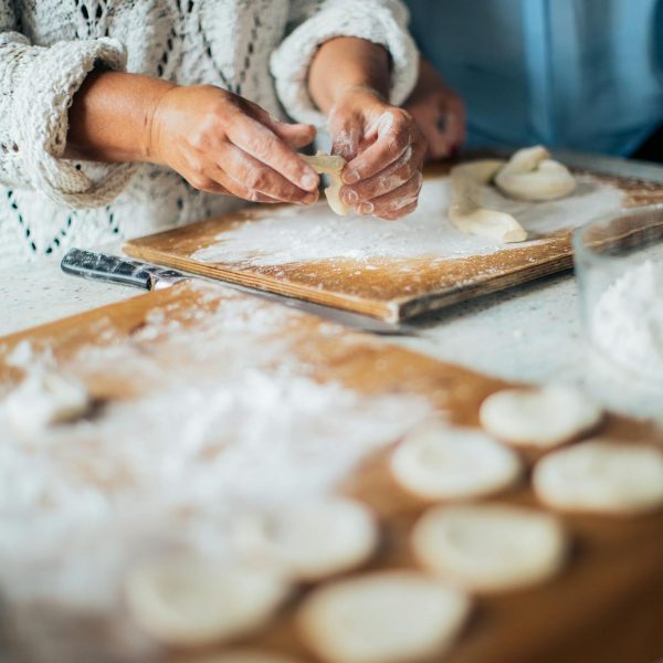 A woman wearing a knitted sweater is skillfully making homemade pastries on a wooden board.