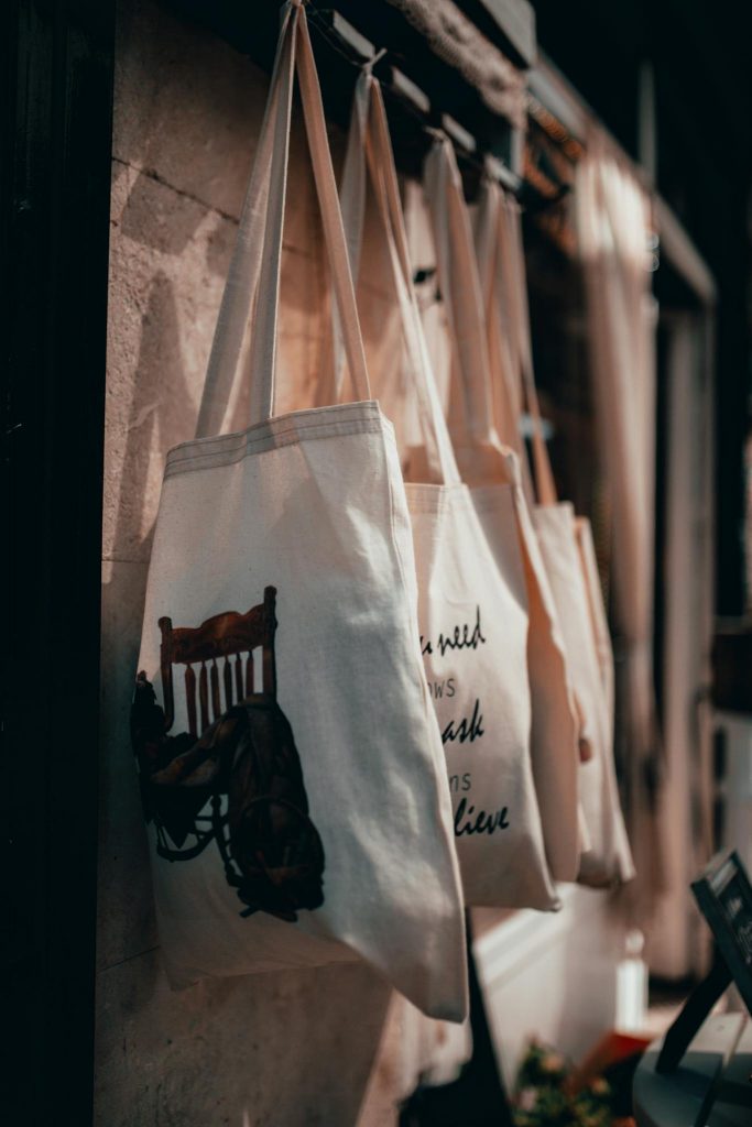 Close-up of canvas tote bags hanging on a rack in a warmly lit store interior.