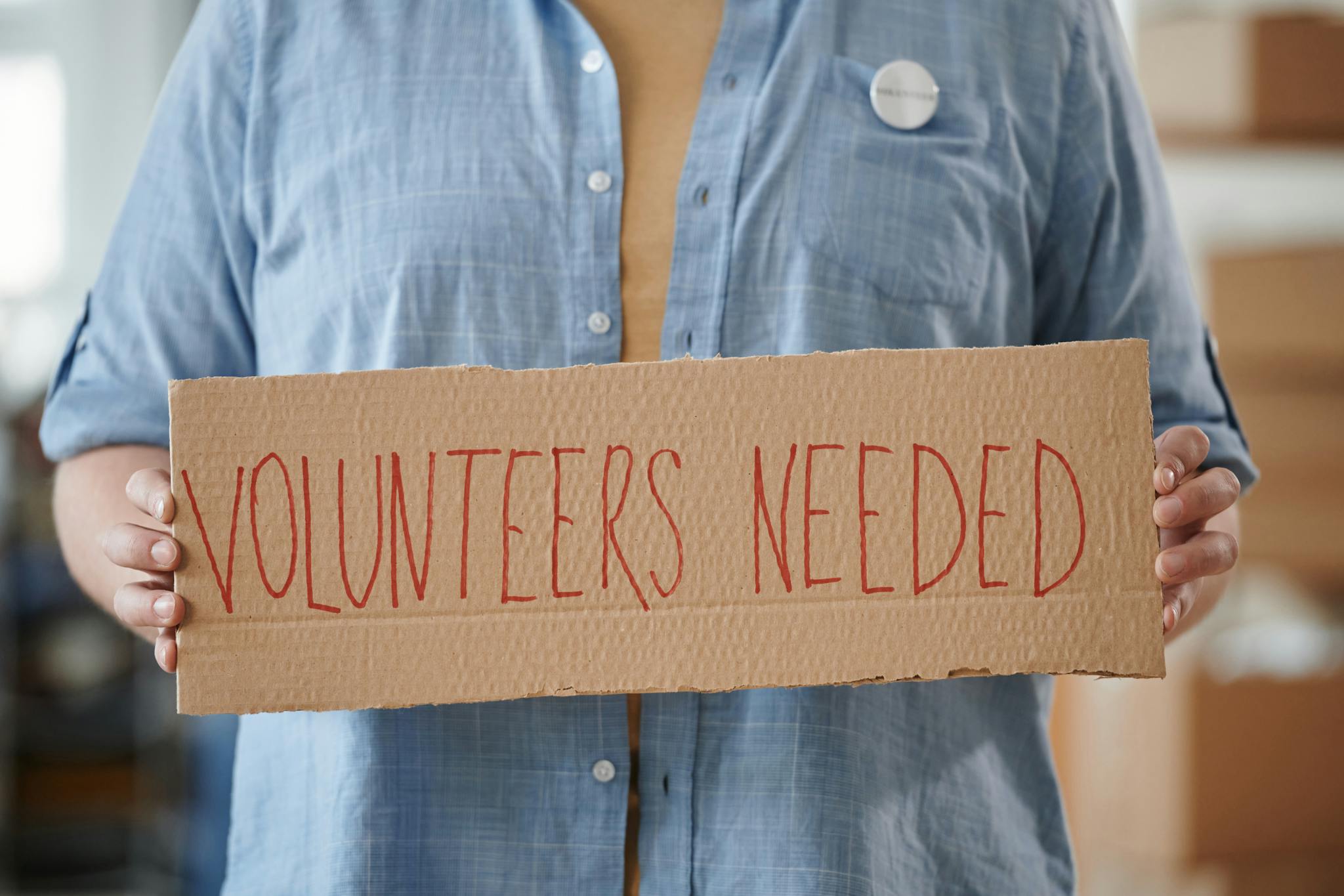 Person holding a sign reading 'Volunteers Needed' to encourage community support.